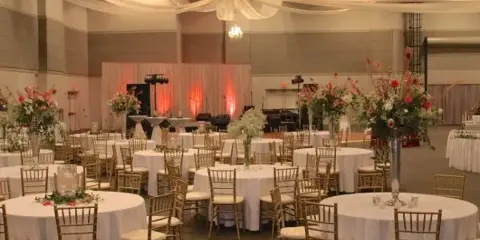 A spacious event hall set up for a wedding reception with round tables, white linens, and floral arrangements.