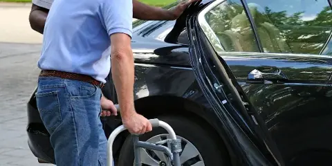 A driver assisting a passenger with a walker into a black sedan