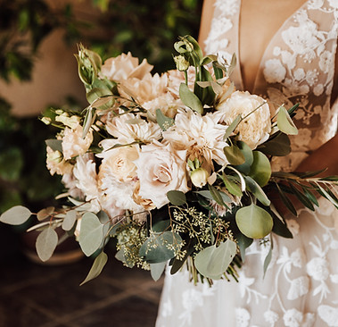 A close-up of a bride holding a bouquet of cream-colored roses, dahlias, and eucalyptus.
