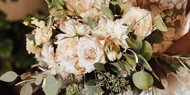 A close-up of a bride holding a bouquet of cream-colored roses, dahlias, and eucalyptus.
