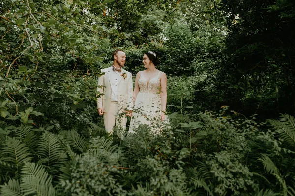A bride and groom standing together in a lush green forest setting.
