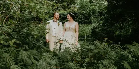 A bride and groom standing together in a lush green forest setting.