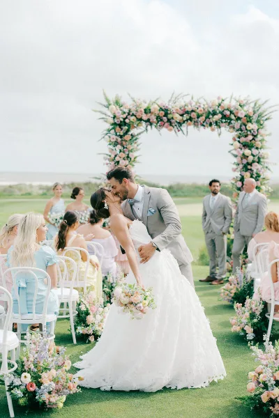 Bride and groom kissing at an outdoor wedding ceremony under a floral arch.