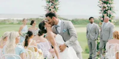 Bride and groom kissing at an outdoor wedding ceremony under a floral arch.