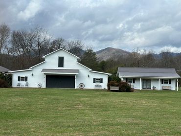 A white barn and adjacent building on a grassy lawn with mountains in the background.