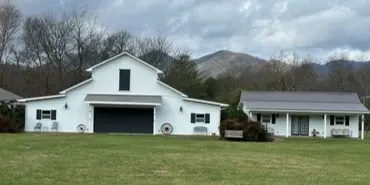 A white barn and adjacent building on a grassy lawn with mountains in the background.
