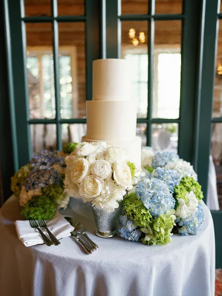 A three-tiered white wedding cake with floral arrangements on a table.