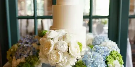 A three-tiered white wedding cake with floral arrangements on a table.