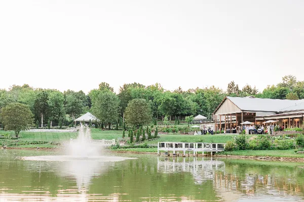 Wide shot of a farm wedding venue featuring a large barn, manicured lawns, and a lake with a fountain.