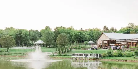 Wide shot of a farm wedding venue featuring a large barn, manicured lawns, and a lake with a fountain.