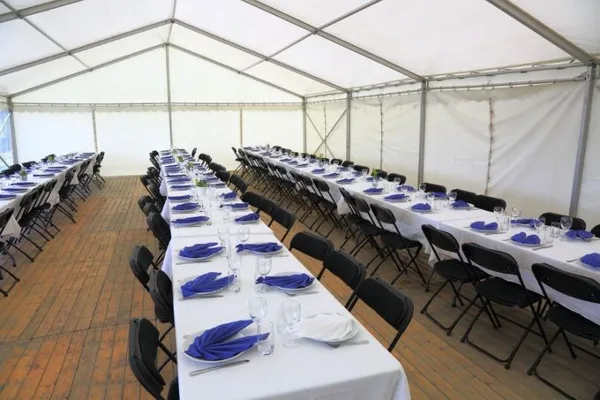 Interior of a large white event tent set up with long banquet tables, black chairs, and blue napkins.