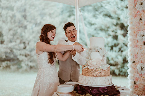 A bride and groom smiling while cutting a decorated three-tier wedding cake.