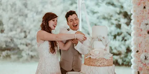 A bride and groom smiling while cutting a decorated three-tier wedding cake.