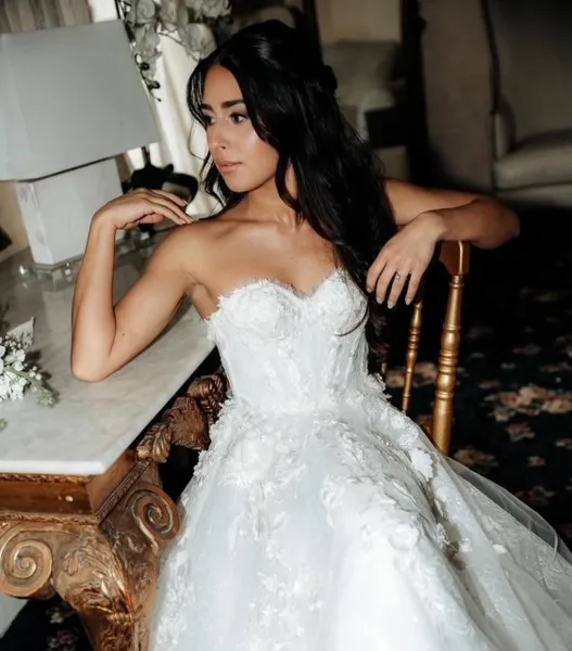 Bride in a white wedding dress with styled hair and makeup sitting on a chair.