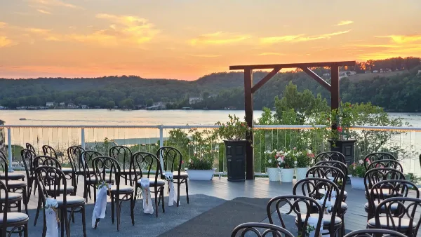 Outdoor wedding ceremony setup with chairs on a lakeside terrace at sunset