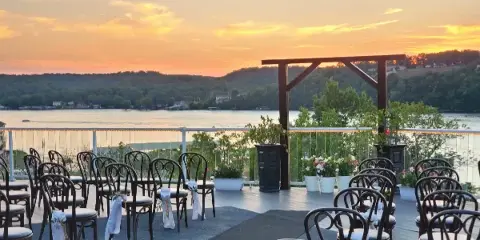 Outdoor wedding ceremony setup with chairs on a lakeside terrace at sunset