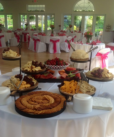 A catering buffet table with assorted appetizers, fruit, and crackers set up in a decorated event hall.