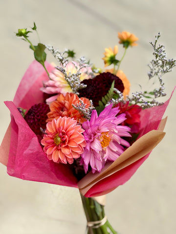 A colorful floral bouquet wrapped in pink paper, featuring daisies and dahlias.