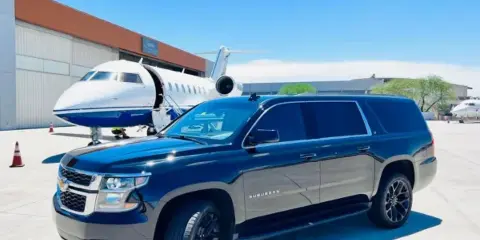 A black luxury SUV parked in front of a private jet at an airport.