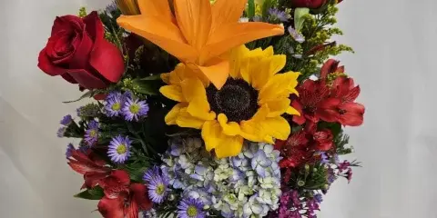 A vibrant floral arrangement with red roses, an orange lily, and a sunflower in a glass vase.