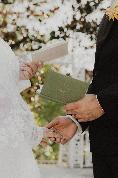 A close-up photograph of a bride and groom holding hands and exchanging vows during a wedding ceremony.