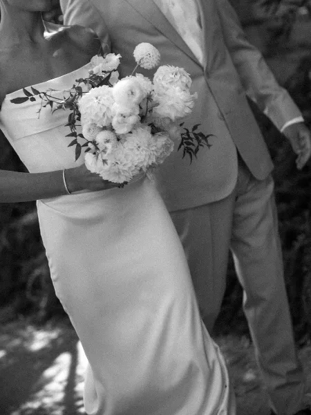 A bride in a white gown holding a large bouquet of white peonies and roses with greenery.