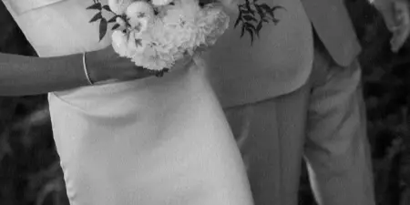 A bride in a white gown holding a large bouquet of white peonies and roses with greenery.