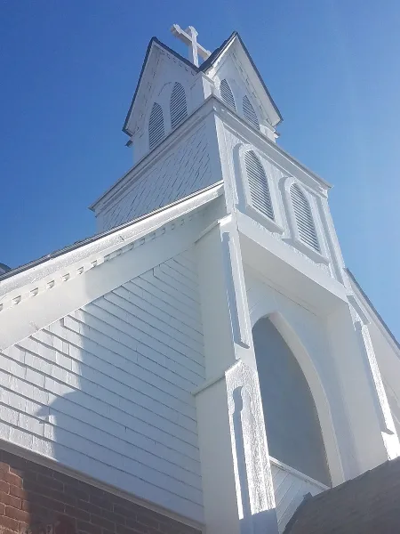 Exterior view of a white church building with a bell tower and cross against a blue sky
