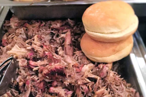 A buffet tray filled with pulled pork and stacked sandwich buns.