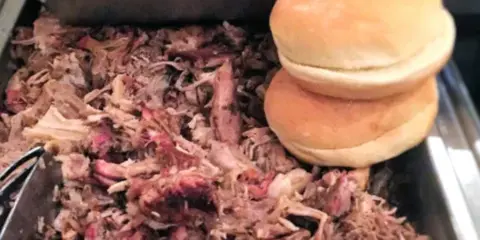 A buffet tray filled with pulled pork and stacked sandwich buns.