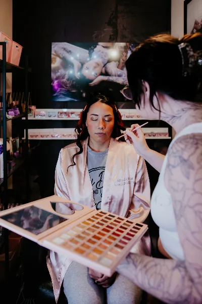 A makeup artist applies makeup to a client wearing an Arielle Roth Makeup Artistry robe in a studio.