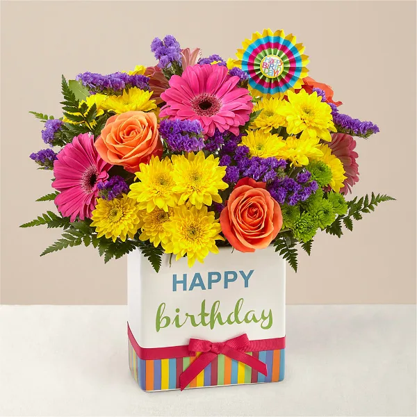 A colorful flower arrangement featuring pink gerberas, yellow chrysanthemums, and orange roses in a white box with a 'Happy Birthday' message.