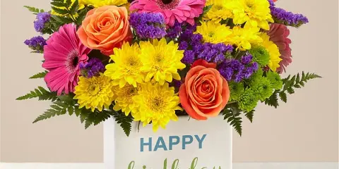 A colorful flower arrangement featuring pink gerberas, yellow chrysanthemums, and orange roses in a white box with a 'Happy Birthday' message.