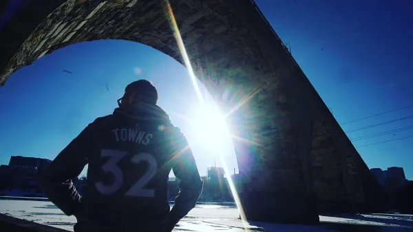 Cinematic low-angle shot of a basketball player wearing a jersey with the name 'TOWNS' and number 32, standing under a bridge with bright sun flare.
