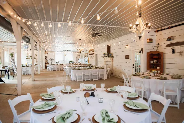 Interior of a rustic barn wedding venue featuring white tables, string lights, and a dance floor.