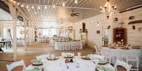 Interior of a rustic barn wedding venue featuring white tables, string lights, and a dance floor.