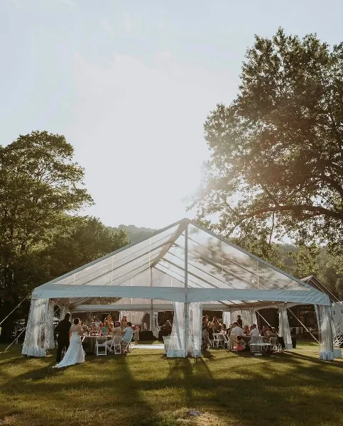A large white event tent set up on a grassy lawn with tables and chairs inside.