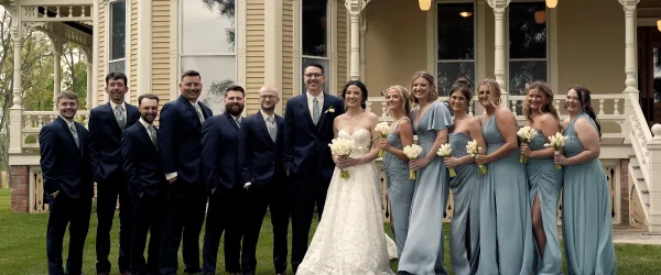 A wedding party consisting of a bride, groom, and attendants posing for a group photo in front of a venue.