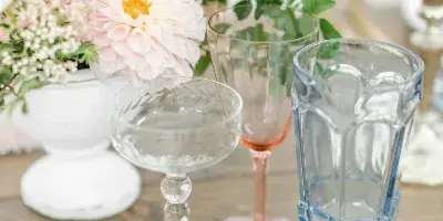 A close-up of a table setting with mixed vintage glassware, gold cutlery, and a floral arrangement.