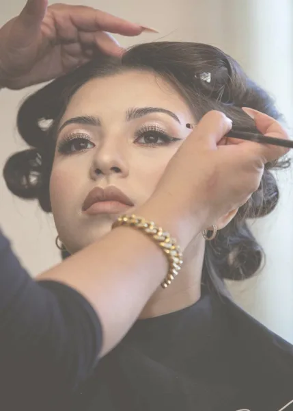 A makeup artist applying eye makeup to a client with an updo hairstyle.