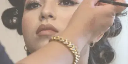 A makeup artist applying eye makeup to a client with an updo hairstyle.
