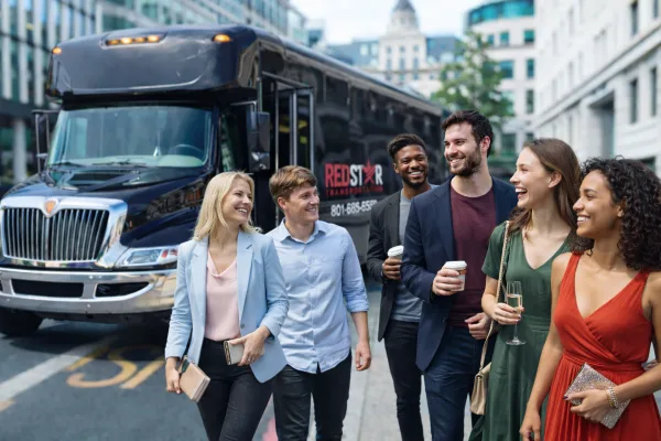 A group of smiling people walking in front of a black Red Star Transportation charter bus.