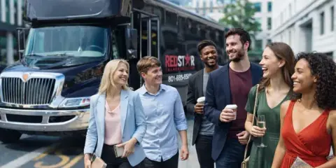 A group of smiling people walking in front of a black Red Star Transportation charter bus.