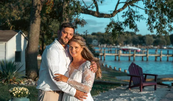 A professional wedding portrait of a bride and groom standing outdoors near a body of water.