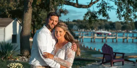 A professional wedding portrait of a bride and groom standing outdoors near a body of water.