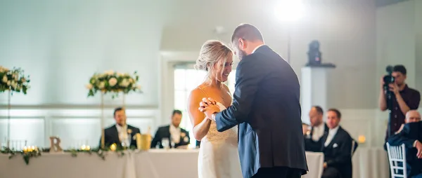 A bride and groom dancing at a wedding reception with guests seated in the background.