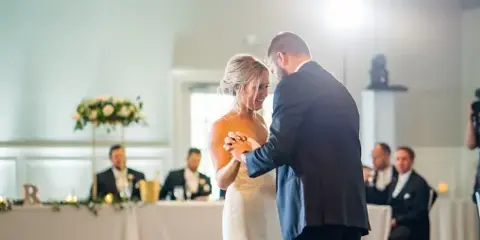 A bride and groom dancing at a wedding reception with guests seated in the background.