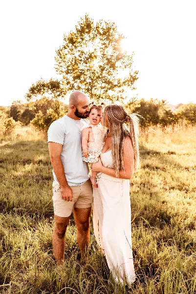 A family of three posing together in a sunlit grassy field during a professional outdoor portrait session.