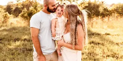A family of three posing together in a sunlit grassy field during a professional outdoor portrait session.