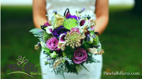A bride holding a vibrant purple and pink wedding bouquet with the Pine Hills Floral Design logo in the corner.